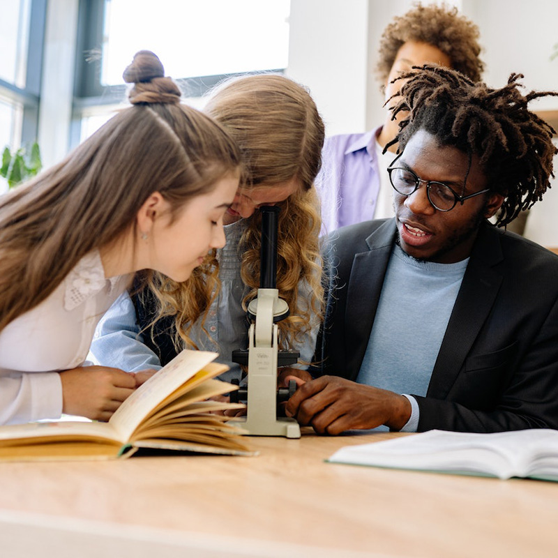 A teacher and students with a microscope