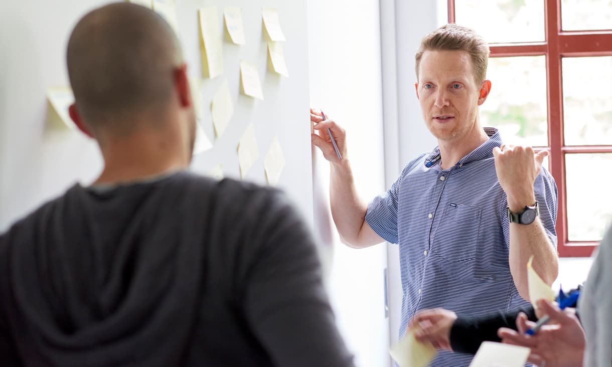 A group of students collaborating at a wall holding post-its.