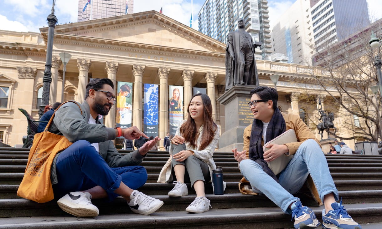 International RMIT students sitting on the steps of an RMIT campus building while facing student presenting in front of board with sticky notes