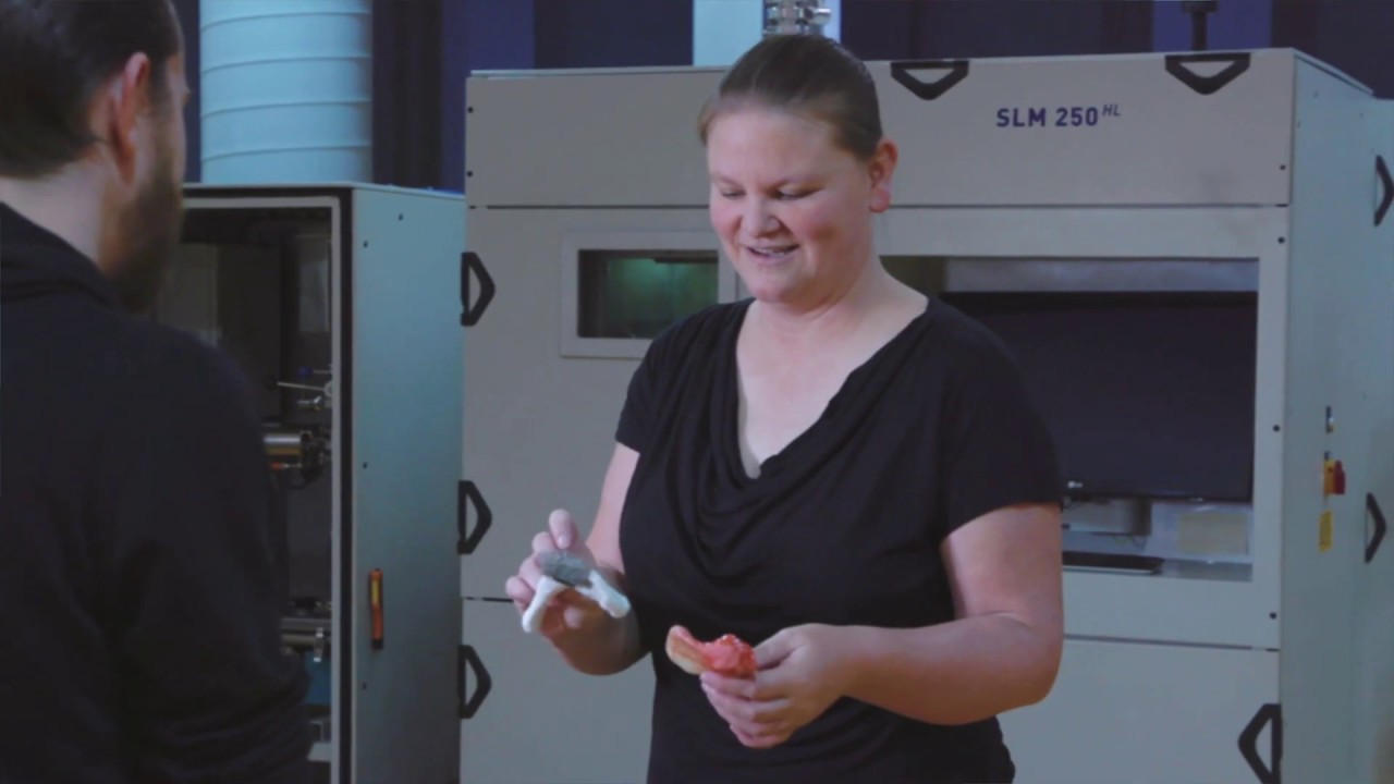 Kate Fox showing two small objects to another student, standing in front of machinery