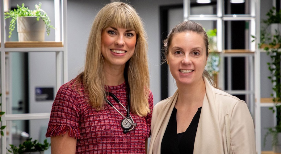 Two women stand in a medical clinic smiling at the camera.