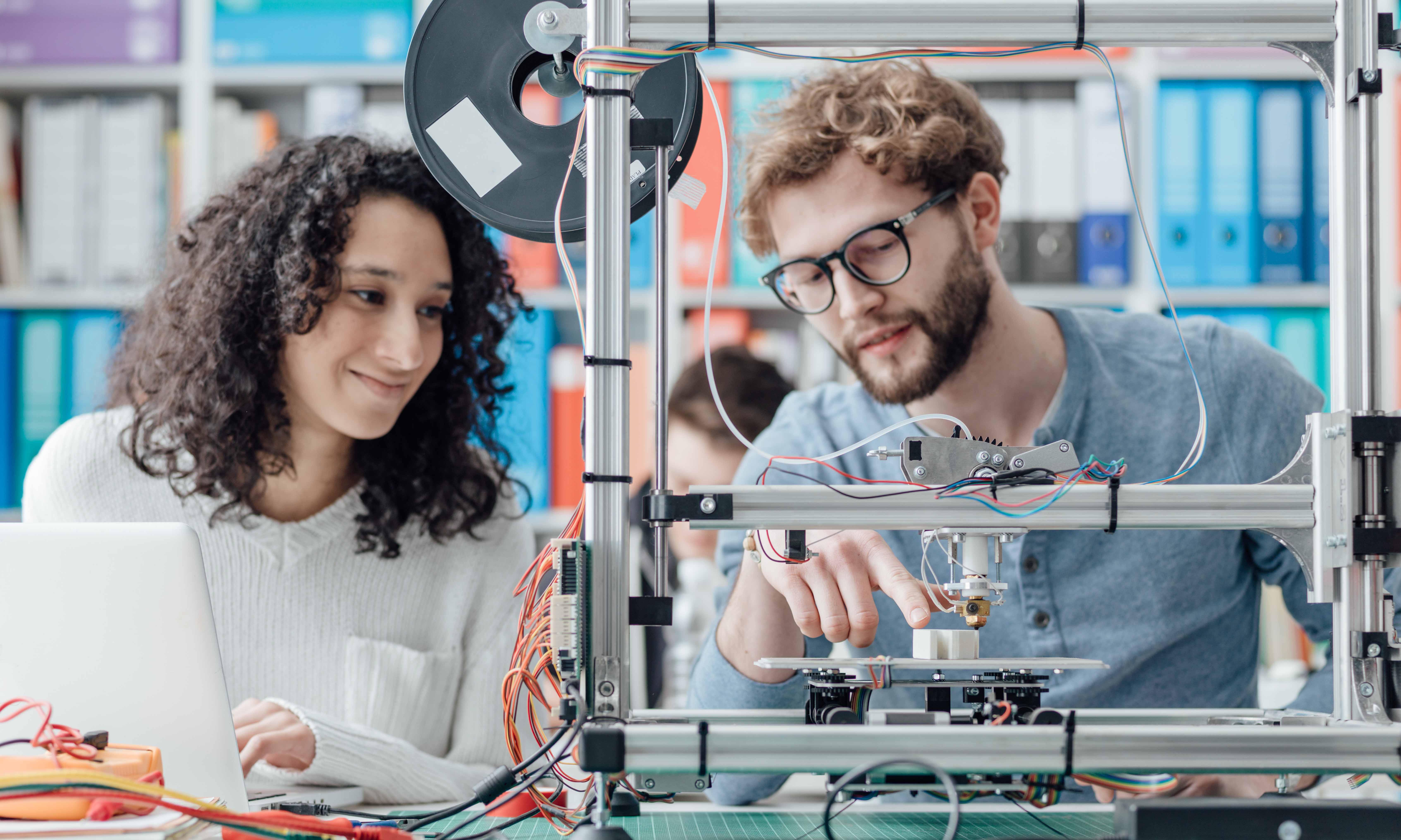 A male and female student working on a mechanical machine and laptop.