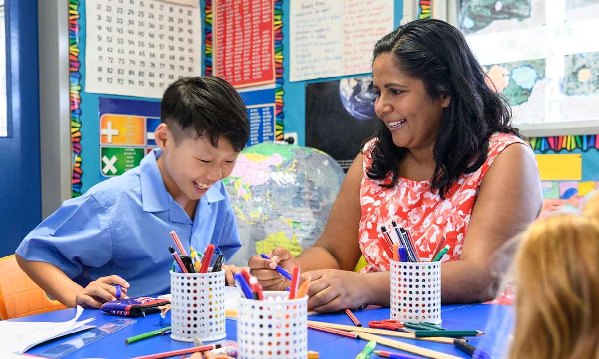 A female Primary school teacher and a young male student sitting at a desk