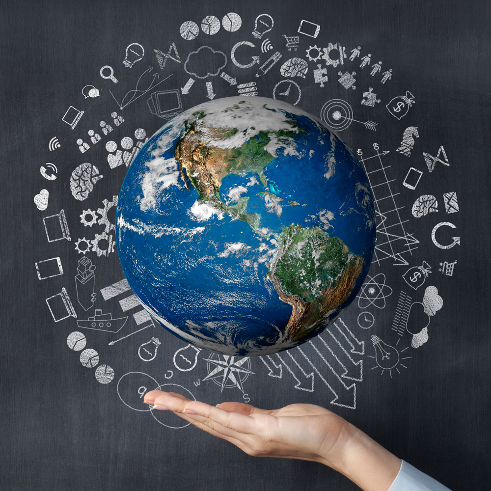 A hand holding a globe with chalk drawings on a blackboard behind